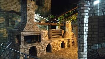 Un edificio de ladrillo con chimenea de piedra, un banco de madera y una pérgola cubierta de plantas trepadoras.