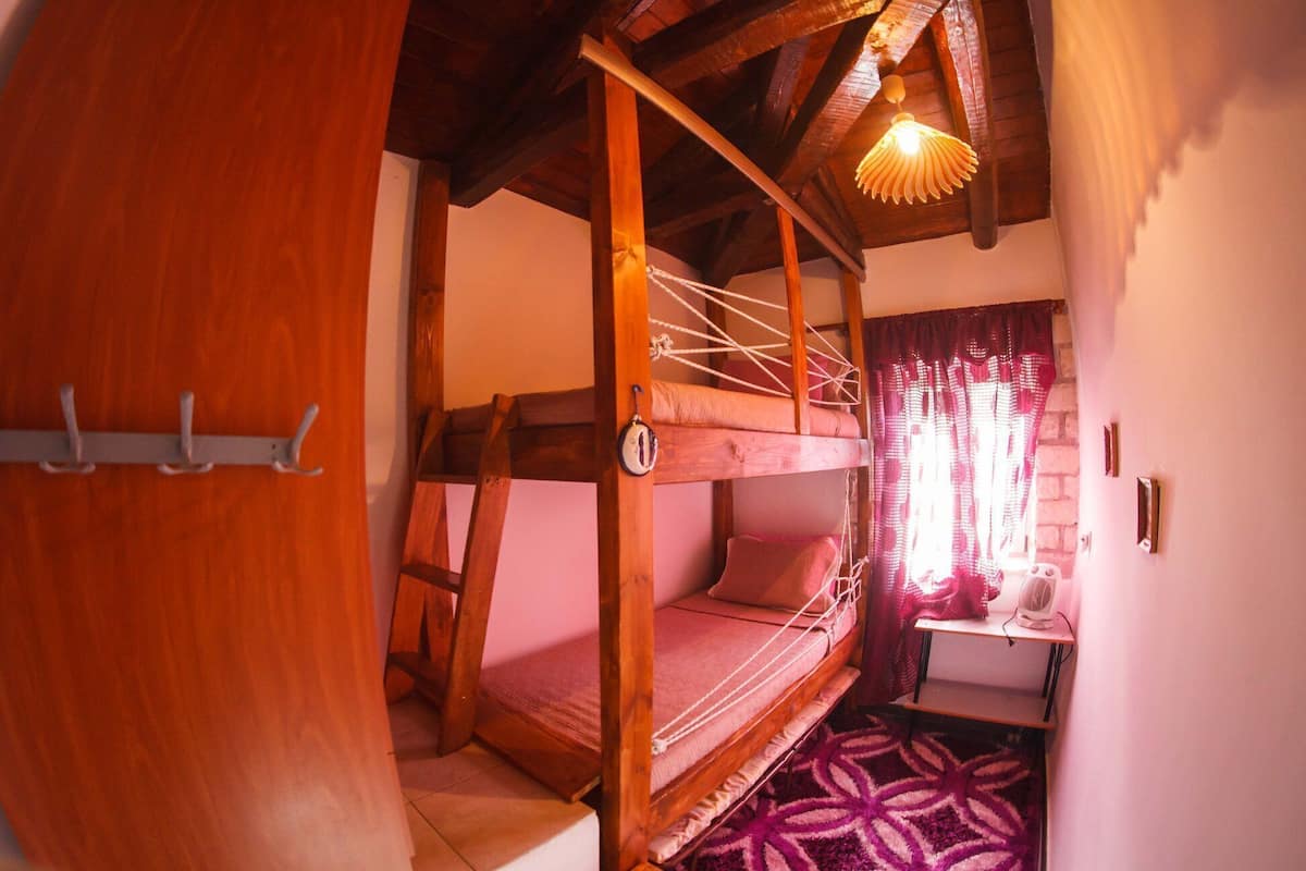 A bunk bed with a wooden frame, a small table with a fan, and a patterned rug.