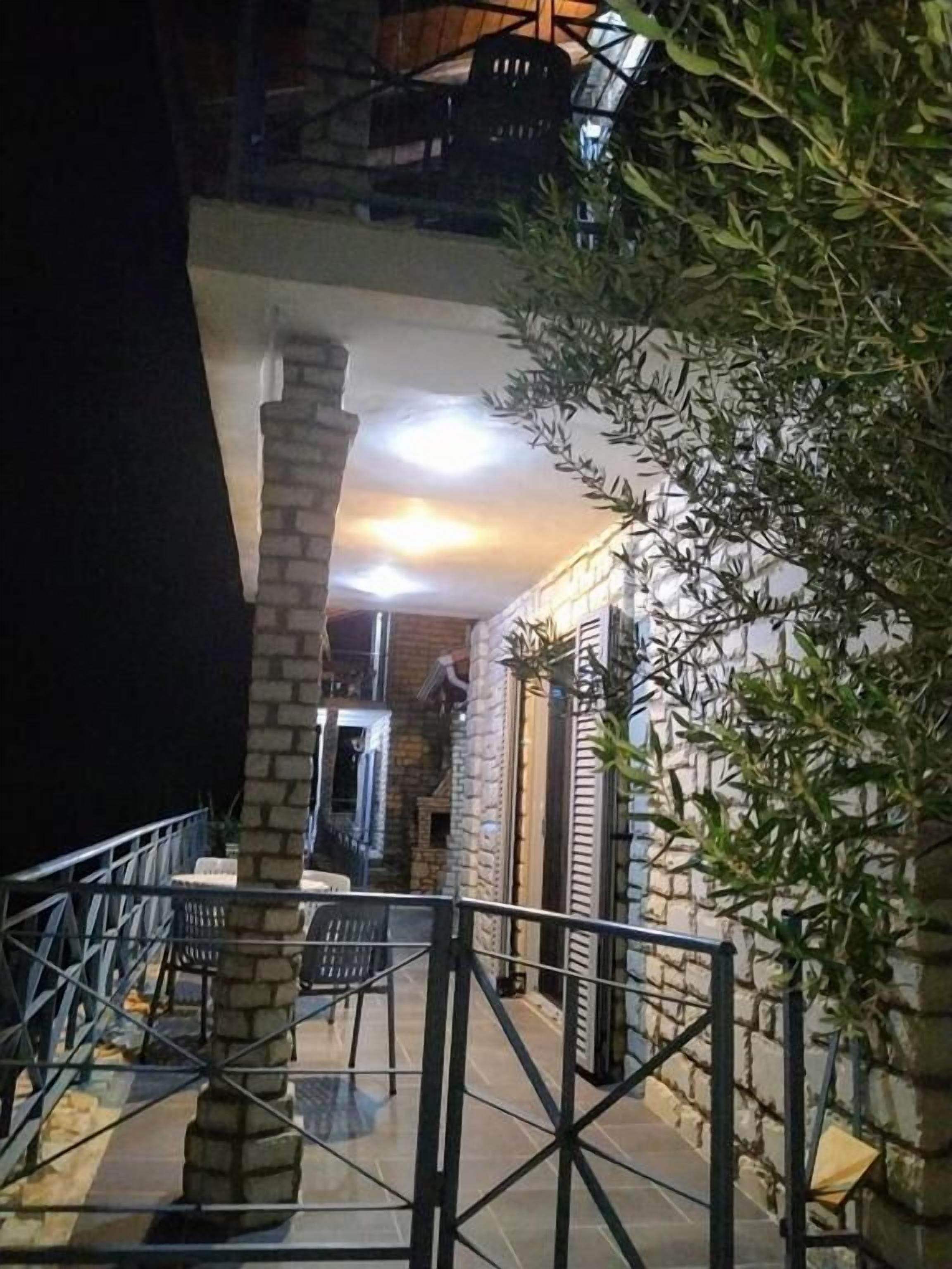 An outdoor area with a stone pillar, a metal railing, and a staircase leading to a balcony.