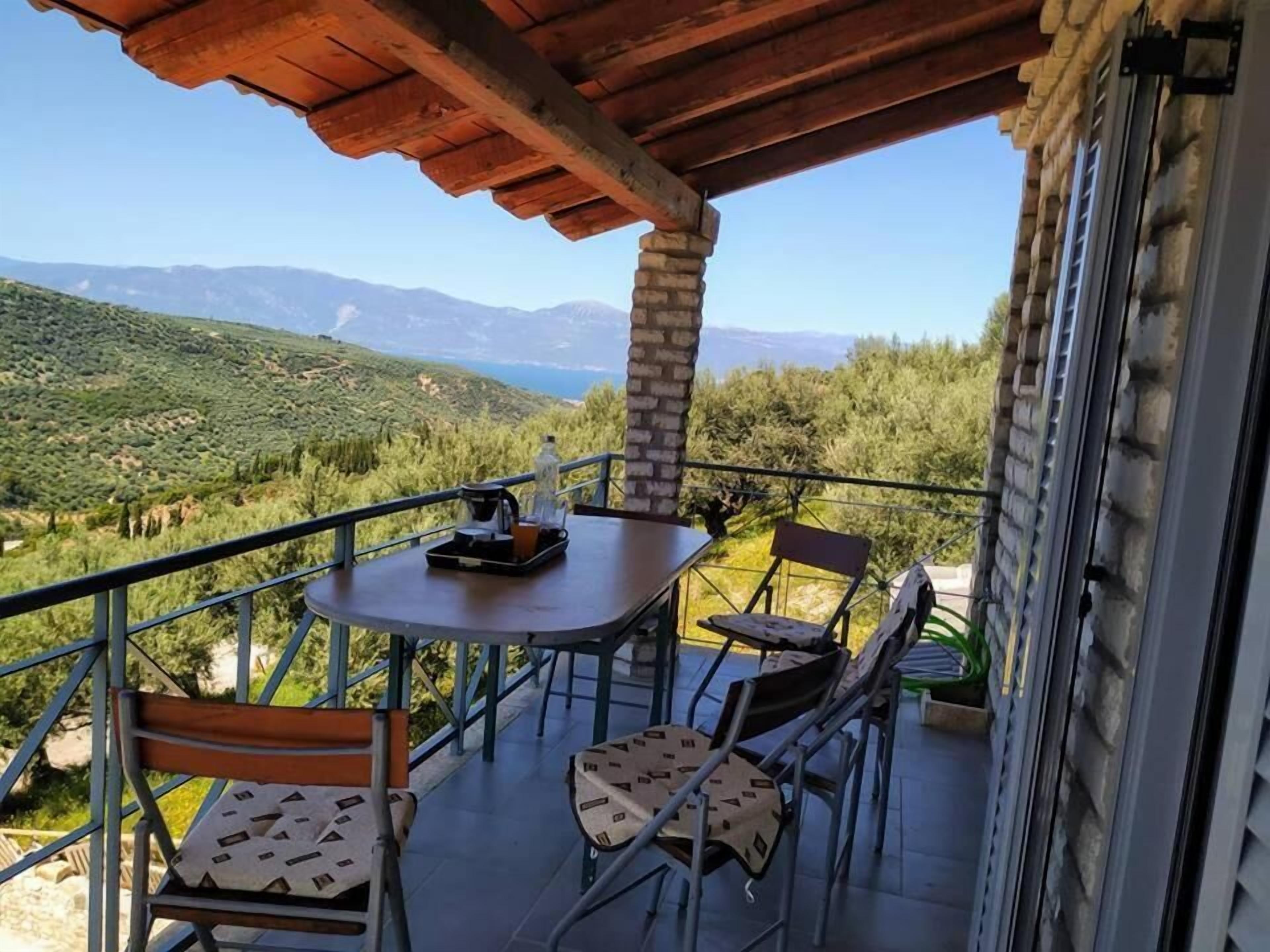 A balcony with a table and chairs, overlooking a mountainous landscape.
