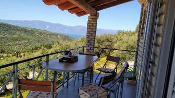A balcony with a table and chairs, overlooking a mountainous landscape.
