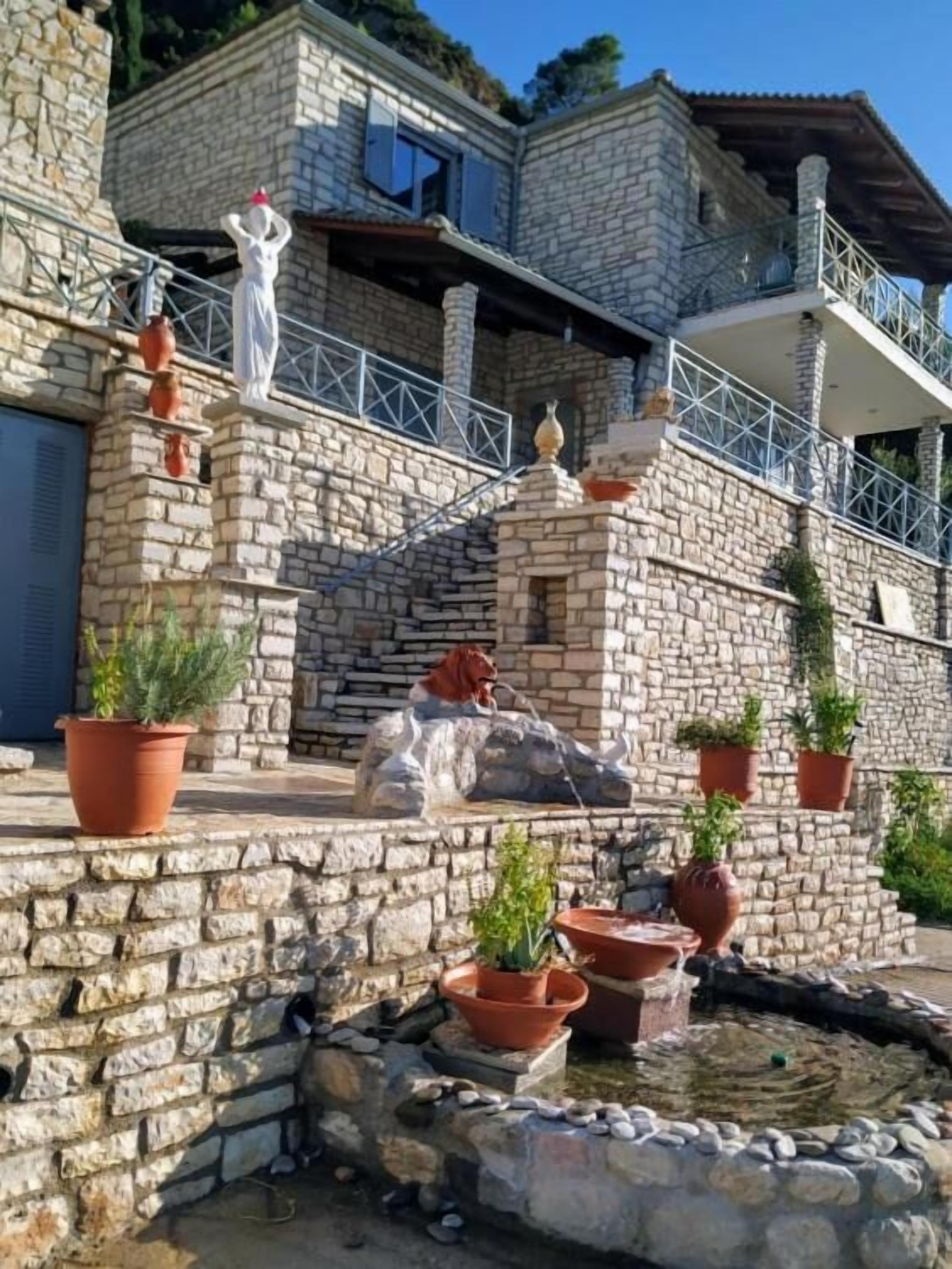 Un bâtiment en pierre agrémenté d’une fontaine, de plantes en pot et d’une statue.