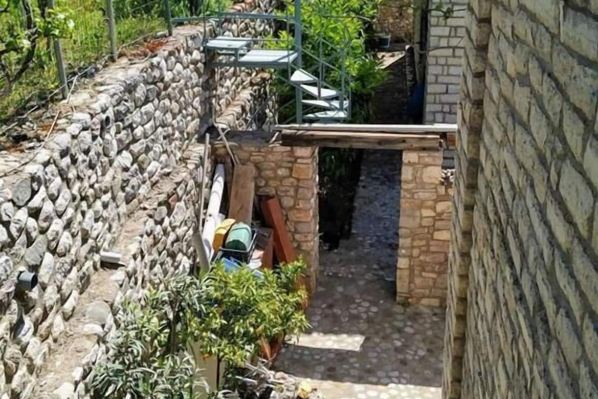 A narrow stone pathway leading to a stone building with a tiled roof.