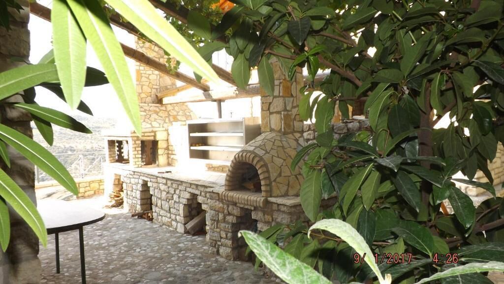 An outdoor stone-built pizza oven and a stone counter, surrounded by greenery.
