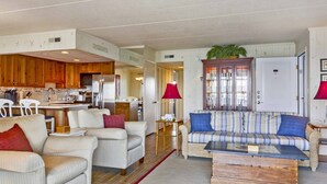 A spacious living area with a sofa set, a coffee table, and a kitchen in the background.