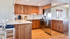 A kitchen with wooden cabinets, stainless steel appliances, and a bar area with stools.