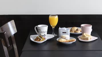 Uma mesa de jantar com um conjunto de café, um copo de suco de laranja e doces.
