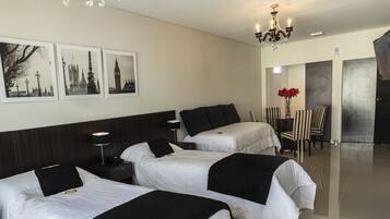 Habitación de hotel con tres camas, un candelabro, zona de comedor y obras de arte en las paredes.