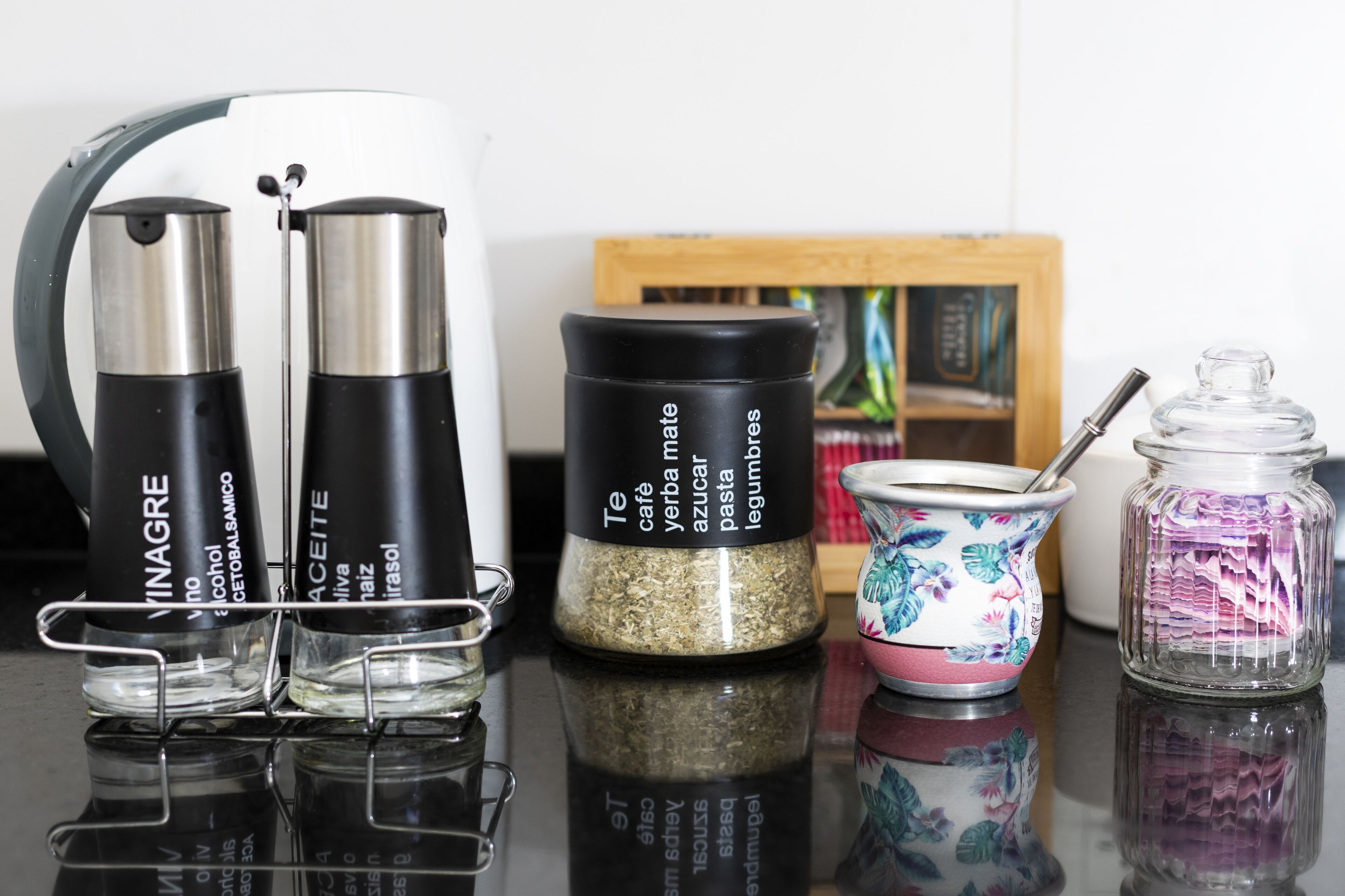 Een keukentrap met een koffiezetapparaat, twee flessen vloeistof, een kruidenpotje, een theepot en een glazen pot met een lepel.