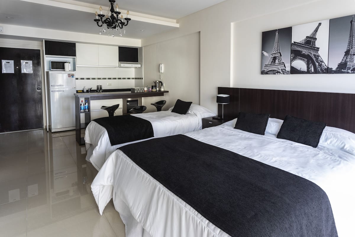 A hotel room with two beds, a kitchenette, a dining area, and a view of the Eiffel Tower.