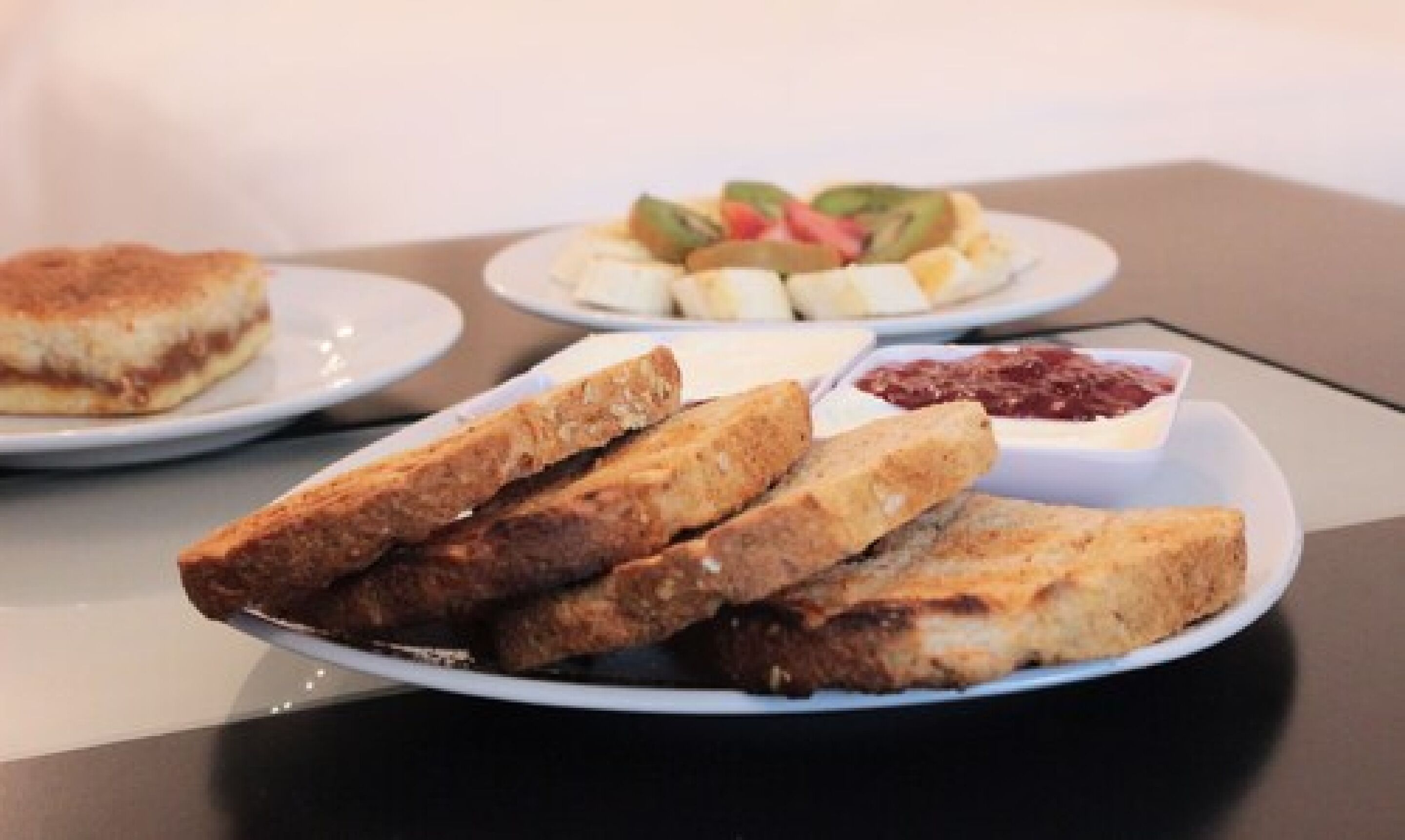Una mesa con platos de comida que incluyen sándwiches, fruta y un cuenco pequeño de mermelada.