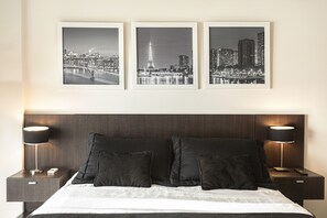 A hotel room with a large bed, two bedside tables, and three black-and-white framed pictures on the wall.