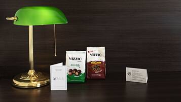 A desk with a green desk lamp, two packages of Vizzio chocolate, a business card, and a no smoking sign.