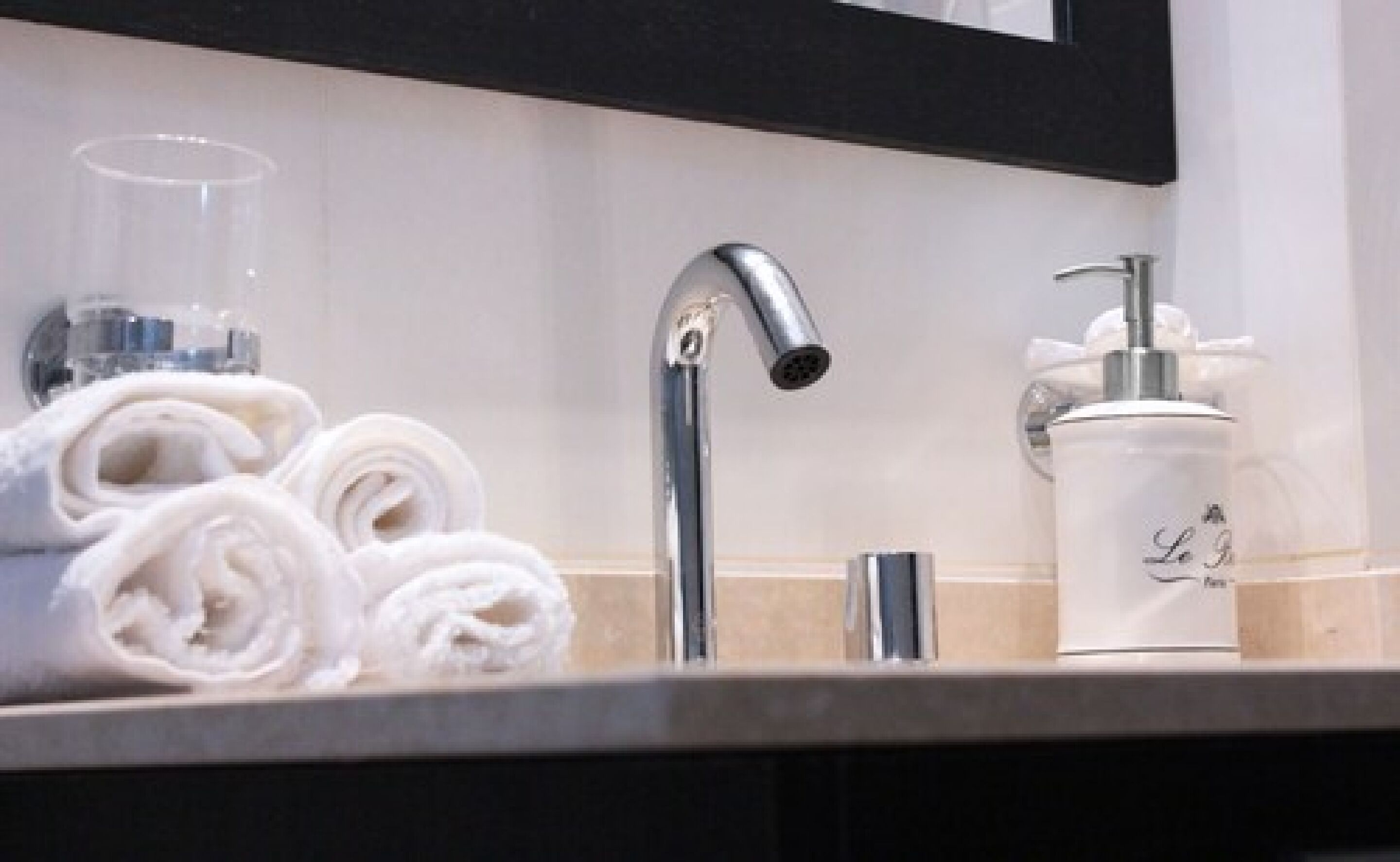 Ein Waschbecken mit Spiegel, Seifenspender und einem Glasbehälter.