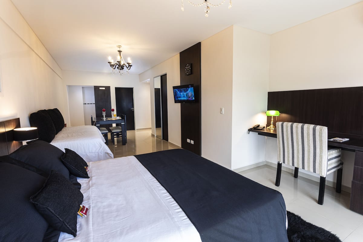 A hotel room with two beds, a desk, a chair, a TV, and a chandelier.