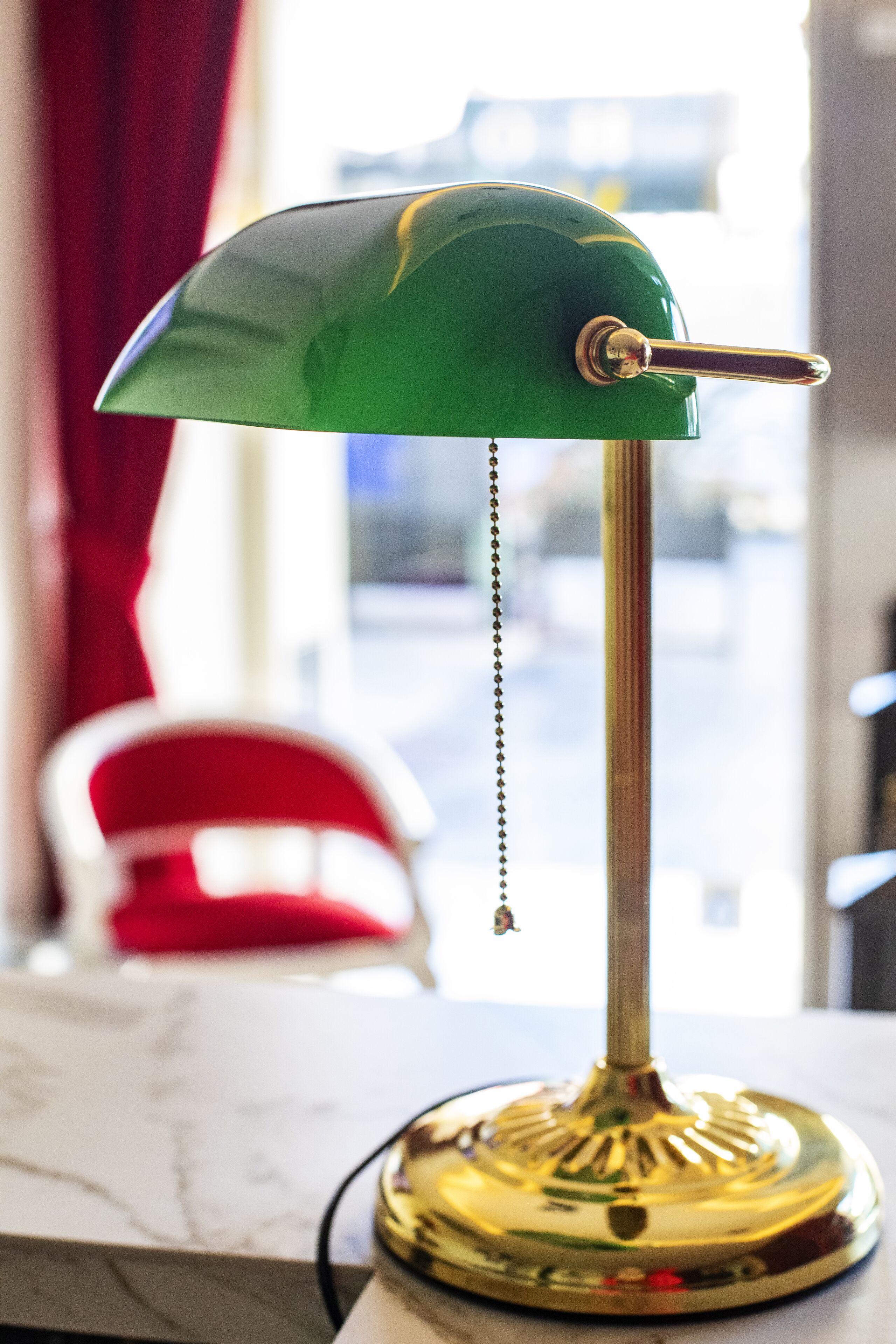 Eine grüne Schreibtischlampe mit metallischem Fuß auf einer Marmorplatte.