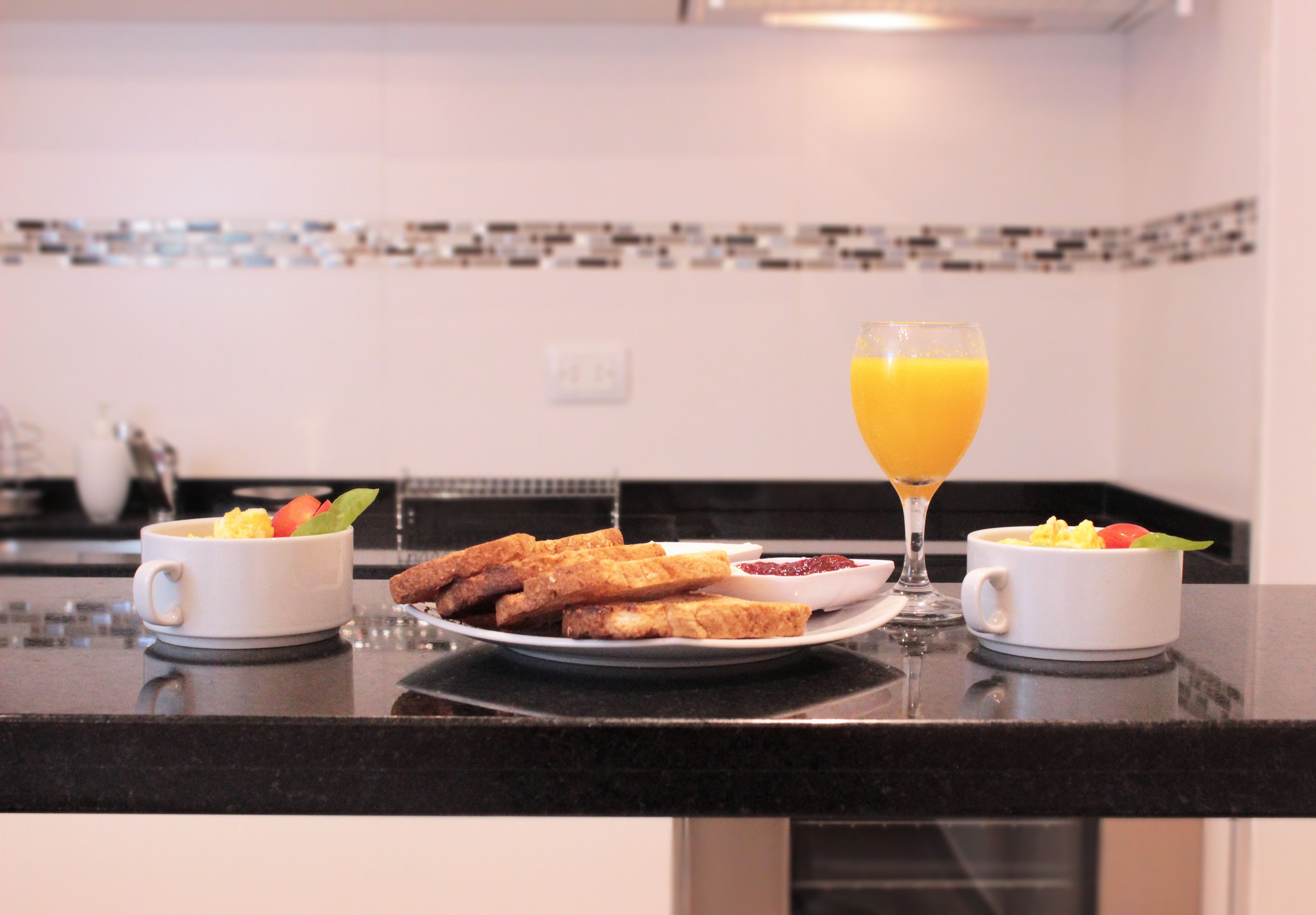 Une table de petit-déjeuner avec des toasts, des fruits et du jus d’orange, le tout disposé sur un comptoir de cuisine.
