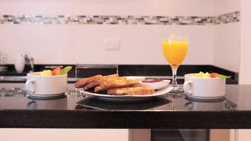 Une table de petit-déjeuner avec des toasts, des fruits et du jus d’orange, le tout disposé sur un comptoir de cuisine.