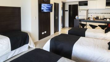 A hotel room with two beds, a TV on the wall, a kitchenette, and a separate dining area.