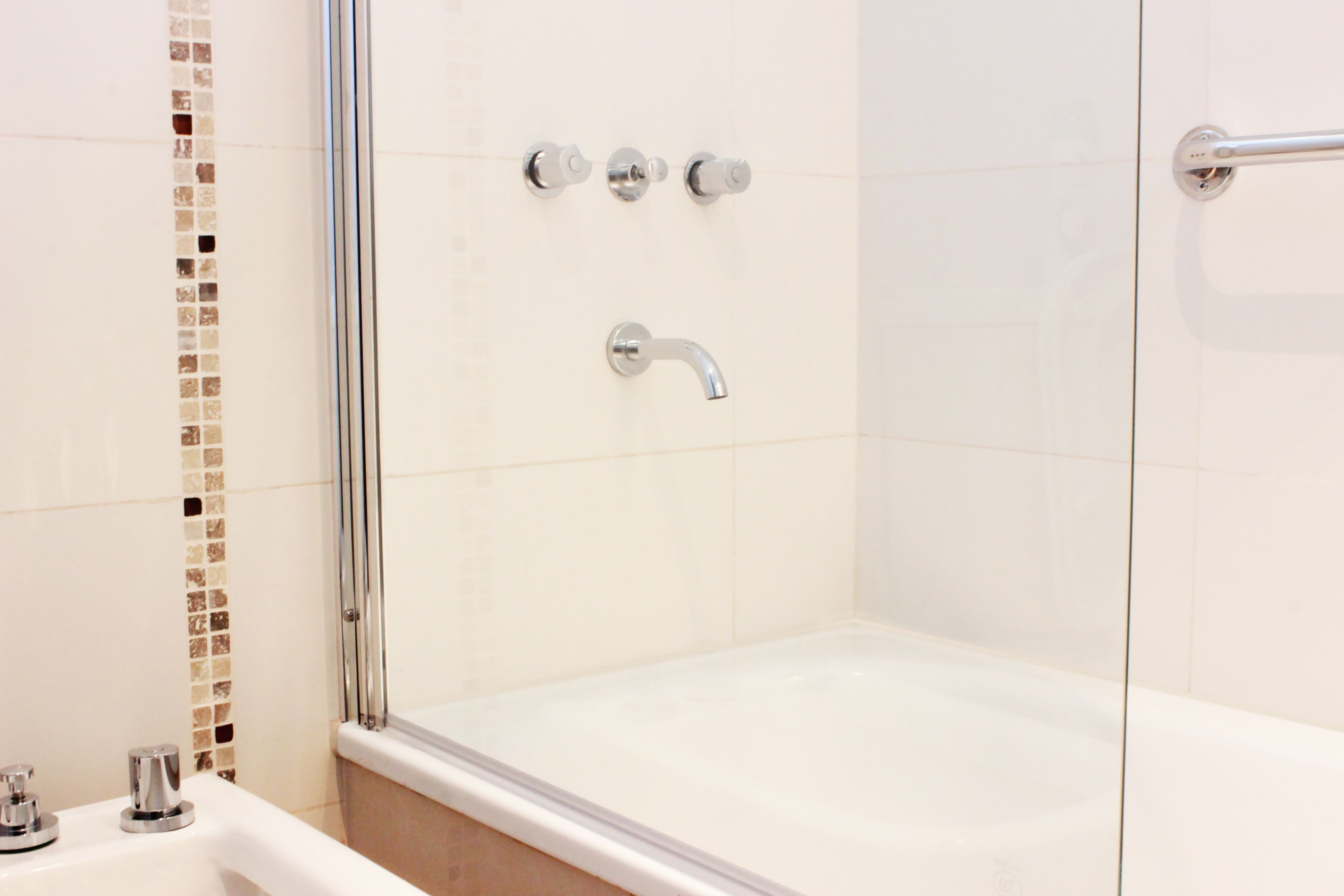 Uma casa de banho moderna com chuveiro envidraçado, uma banheira branca e um revestimento de azulejos com detalhes decorativos.