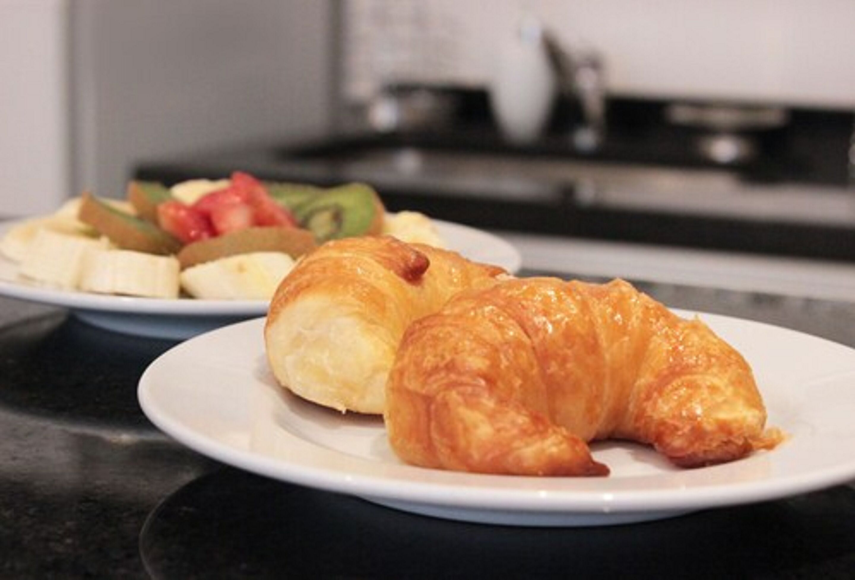 Eine Küchenarbeitsplatte mit einer Platte Croissants und einer Platte Obst.