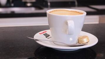 Una taza blanca de café con una cuchara sobre un plato, colocada en una encimera negra.