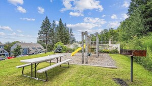 Un parque infantil con tobogán y estructuras para escalar, rodeado de una mesa de picnic y un buzón.