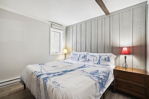 Une chambre à coucher comprenant un lit, une table de chevet, une lampe, une fenêtre et un mur recouvert de panneaux de bois verticaux.