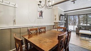 Un comedor con mesa y sillas de madera, una araña, chimenea y un ventanal con vistas a árboles.