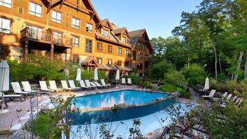 A pool area with lounge chairs and umbrellas, surrounded by a wooden building with balconies.