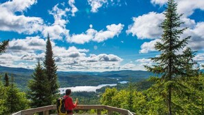A person standing on a wooden observation deck with a clear view of a lake and mountains in the distance. - BEST Ski-in / ski-out in Tremblant!!!  CHIC chalet overlooking ski slopes!
   
  (Mont-Tremblant)
