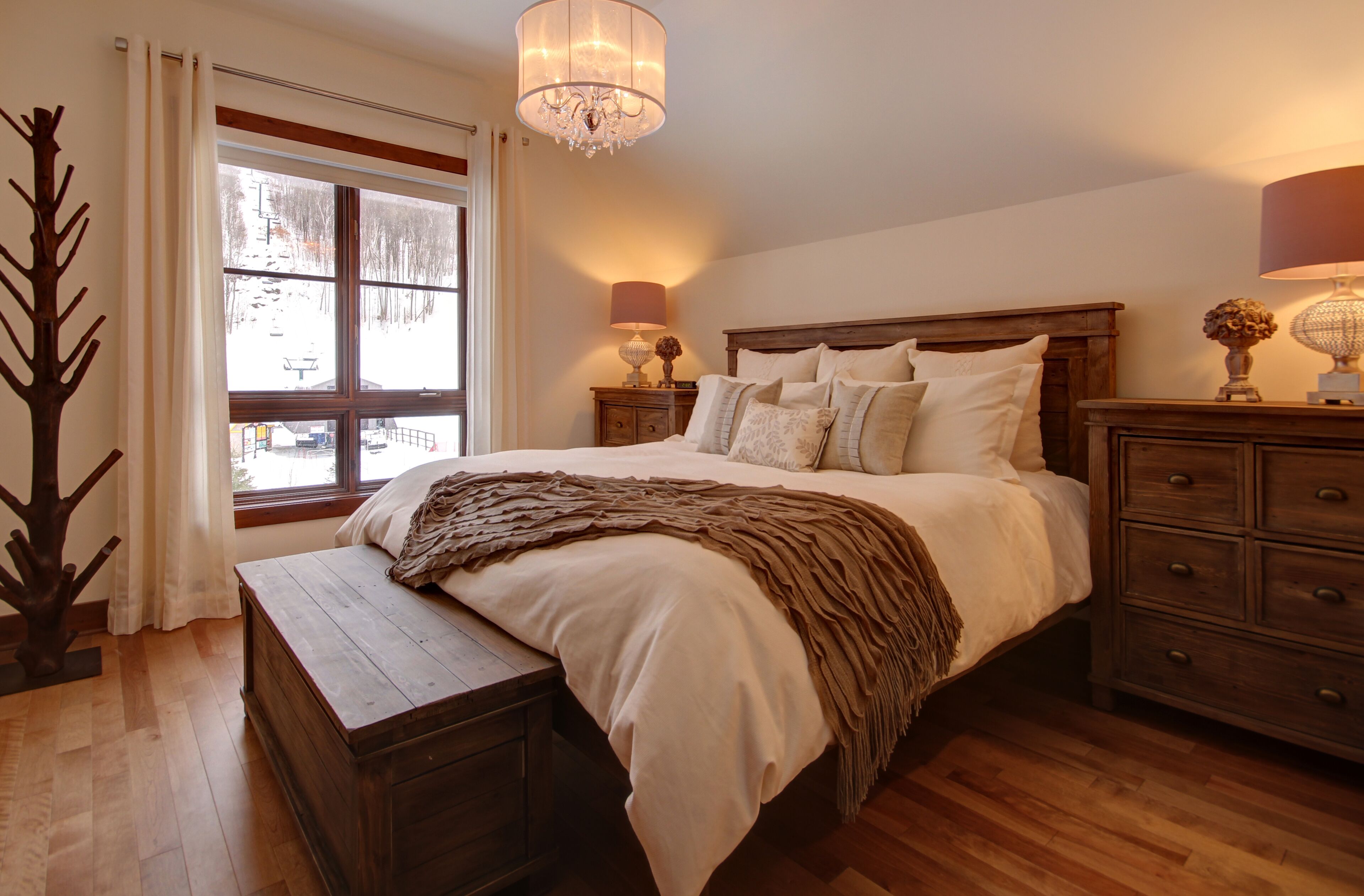 Une chambre à coucher avec un lit en bois, une table de chevet avec une lampe, une commode et une fenêtre avec des rideaux.
