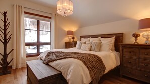 A bedroom with a wooden bed, a nightstand with a lamp, a dresser, and a window with curtains. - BEST Ski-in / ski-out in Tremblant!!!  CHIC chalet overlooking ski slopes!
   
  (Mont-Tremblant)