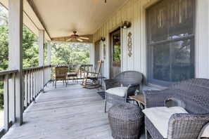 Un porche cubierto con muebles de mimbre, ventilador de techo y vistas al exterior.