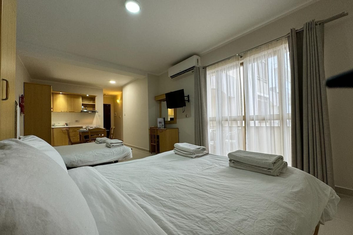Camera d'albergo con due letti, angolo cottura, televisione e finestra con tende.