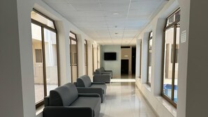 A hallway with a row of grey sofas, large windows, and a flat-screen TV on the wall. - Triton (St. Paul's Bay)