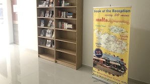 A library with bookshelves and a promotional poster for Malta Sightseeing tours. - The Triton (St. Paul's Bay)