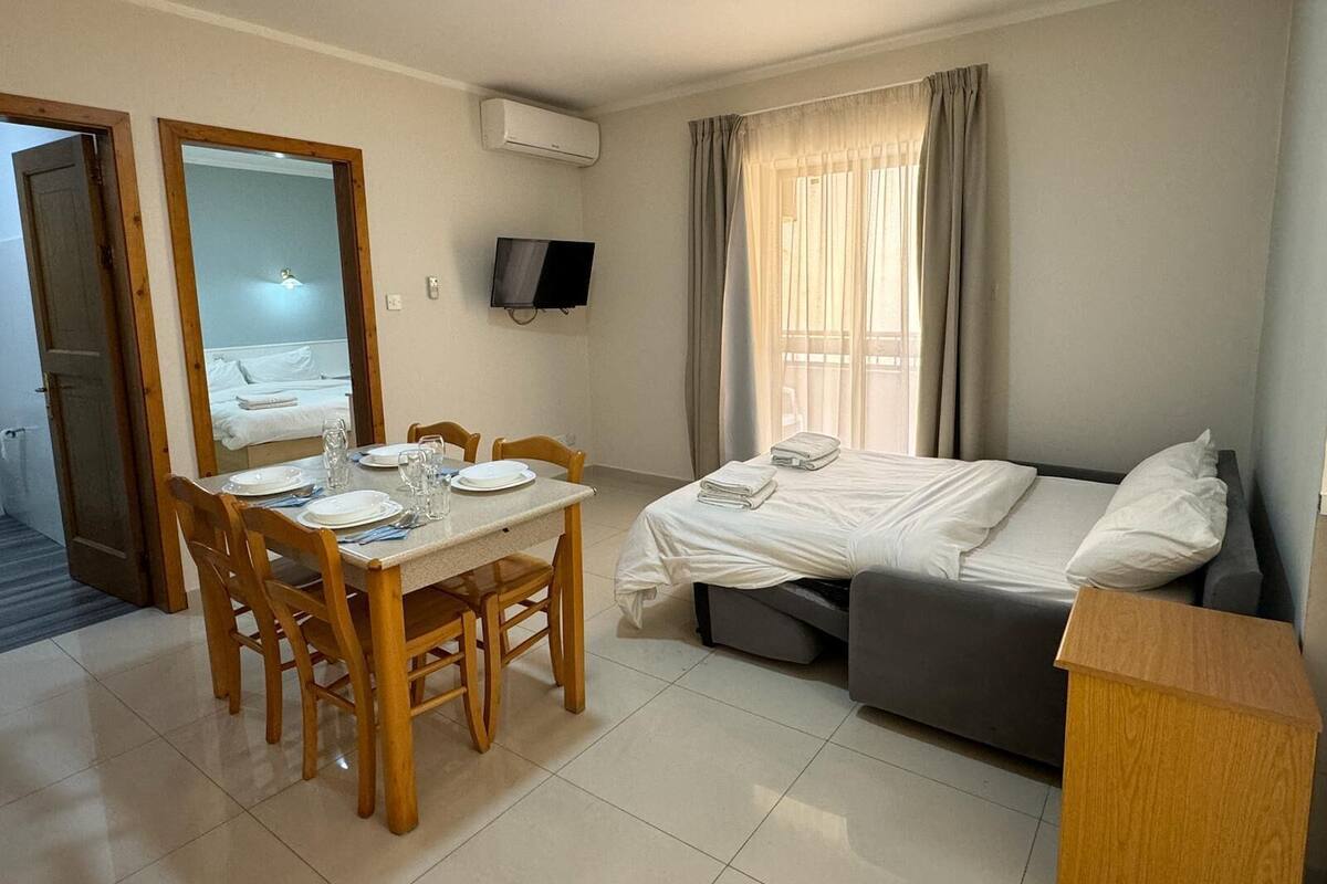 Camera d'albergo con un letto, un piccolo divano, un tavolo da pranzo con sedie, una TV e una finestra con tende.