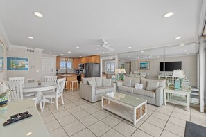 Un grand espace de vie comprenant une table à manger, deux canapés, une table basse et une cuisine à l’arrière-plan.