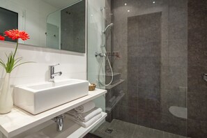 Ein modernes Badezimmer mit einem weißen Waschbecken, einer Duschkabine aus Glas und einem Spiegel über dem Waschbecken.