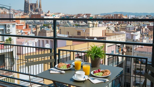 A balcony with a table set for breakfast, overlooking a cityscape with buildings and a construction site. - Tessa - Habitat Apartments (Barcelona)