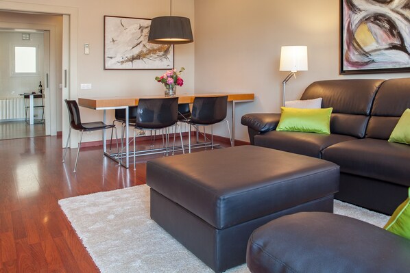A modern living room with a leather sofa, a dining table with chairs, and a coffee table. - Tessa - Habitat Apartments (Barcelona)