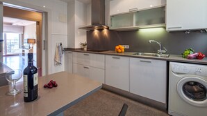 A modern kitchen with a wine bottle, a glass, and fruits on the counter. - Tessa - Habitat Apartments (Barcelona)