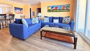 Una sala de estar con un sofá seccional azul, una mesa de centro de madera y un cuadro de globos aerostáticos en la pared.