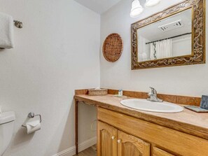 A bathroom with a wooden vanity, a white sink, a mirror with an ornate frame, a towel rack, and a wall-mounted basket.