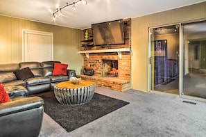 Ein Wohnzimmer mit Ledersofa, rundem Couchtisch, Kamin und einer Glastür zum Balkon.