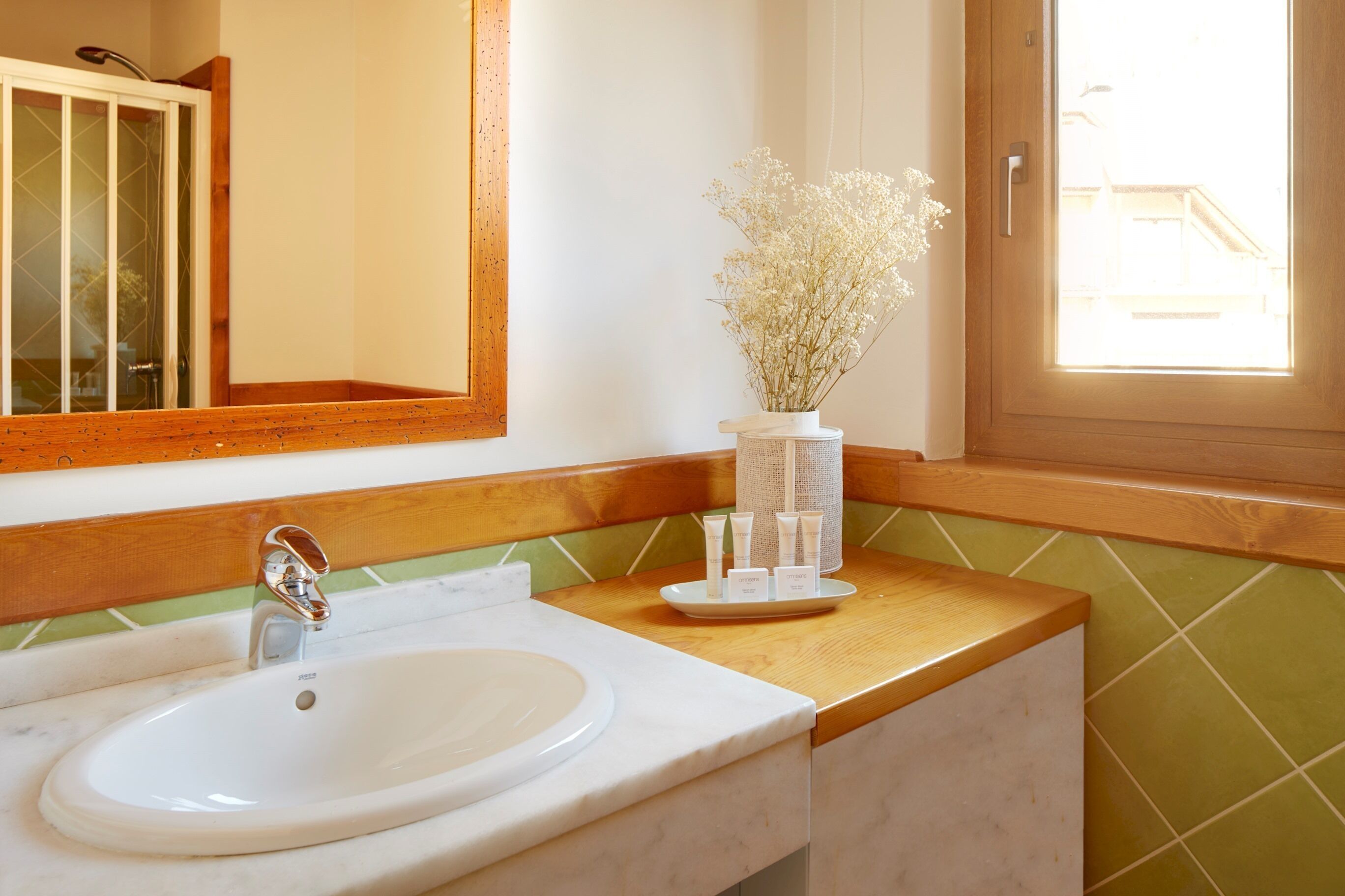 Une salle de bain avec un lavabo blanc, un meuble-lavabo en bois, un miroir et une fenêtre donnant sur un beau paysage.