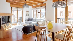 A spacious living area with wooden flooring, a stone fireplace, a sofa, and a dining table with chairs.