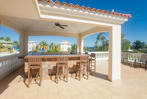 Relax in a serene outdoor space with a bar and seating, surrounded by palm trees and a beautiful view.