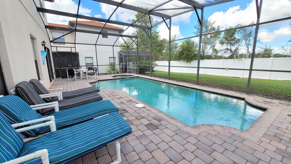A covered outdoor swimming pool with lounge chairs and a patio table. - Executive Home in Gated Community w pool spa, games room, close to shops (Clermont)